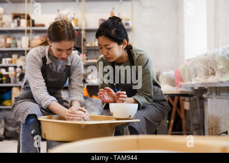 Qualifizierte asiatischen Potter in Schürze Lehre junge Frau Ton Vase auf Keramik Rad in der modernen Werkstatt zu machen, Töpferkurs Stockfoto