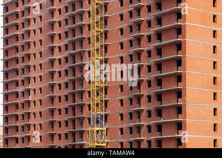 Close-up auf ein mehrstöckiges Wohnhaus im Bau aus rotem Backstein mit einem Teil von einem gelben Kran. Die Wände des Hauses in den Prozess Stockfoto