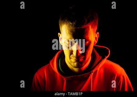 Ein erwachsener Kerl steht mit seinem Kopf gekippt und schauen nach unten in einem orange Hooded Sweatshirt in Rot und Gelb auf der Seiten mit einem nachdenklich und Re Stockfoto