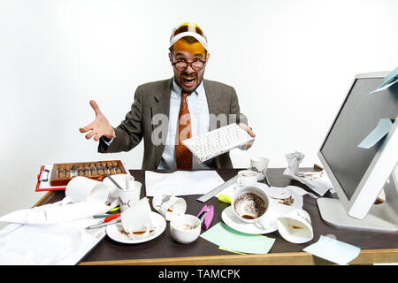 Konstanter Ausfall. Junger Mann verschüttete Getränke auf der Tastatur während der Arbeit und versucht aufzuwachen. Eine Menge Kaffee trinken. Konzept der "büroangestellter tr Stockfoto