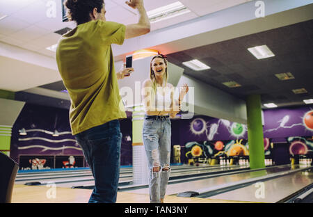 Junger Mann Aufnahme Frau spielen Bowling im Club. Junge Freunde genießen, spielen bei Bowling Arena. Stockfoto