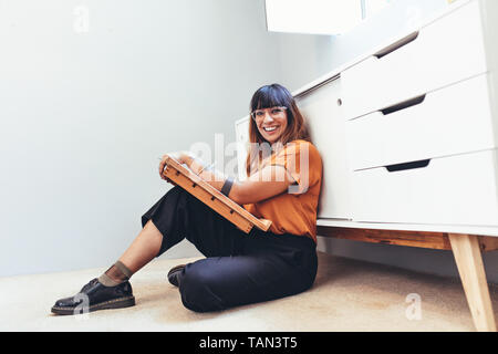 Weibliche Illustrator eine Zeichnung auf dem Boden sitzen in Ihrem Büro. Kreative Künstlerin sitzt auf dem Boden mit einer Zeichnung pad und Designs. Stockfoto