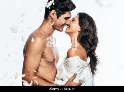 Seitenansicht des liebevollen jungen Paar Küssen mit Federn um fallen. Liebevoller Mann und Frau genießen einen besonderen Augenblick auf einem weißen Hintergrund. Stockfoto