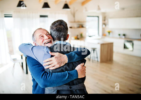 Ein erwachsener hipster Sohn und Vater in Innenräumen zu Hause, umarmen sich. Stockfoto