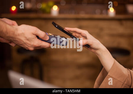 7/8 Bild der Frau Bezahlen mit Handy Technologie in einem Coffee Shop. Frau mit Handy. Kunden barista zu bezahlen. Stockfoto