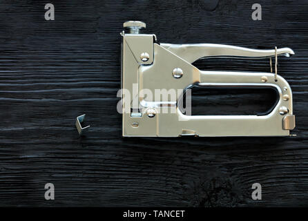 Metal Industrial Chrom Tacker und Klammern, um es auf einem schwarzen Holztisch mit der Textur von altem Holz liegen. Stockfoto