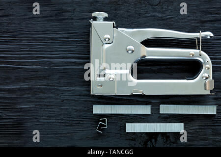 Metal Industrial Chrom Hefter und Kassette klammern, um es auf einem schwarzen Holztisch mit der Textur von altem Holz liegen. Stockfoto