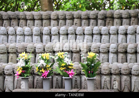 Stein Statuen des Ksitigarbha (Jizo Bosatsu), Hasedera (Hase-dera) Tempel, Kamakura, Japan. Fokus auf Blumen Stockfoto