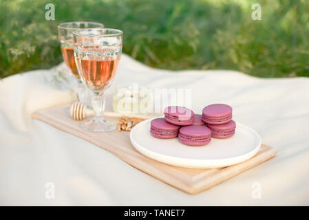 Rosa und Pink französische Makronen oder Makronen mit Glas Becher rosa Wein in einer Runde weiße Platte auf eine beige Tischdecke Hintergrund Stockfoto