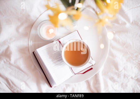 Freah Tasse grünen Tee bleiben auf offenes Buch im Bett mit Blumen und Kerzen Nahaufnahme. Guten Morgen. Top vew. Stockfoto