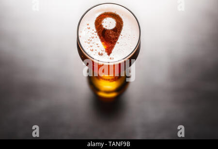 Lokale Bier Konzept. Lage pin Symbol auf Bier Glas Schaum auf schwarz Tabelle, Ansicht von oben Stockfoto