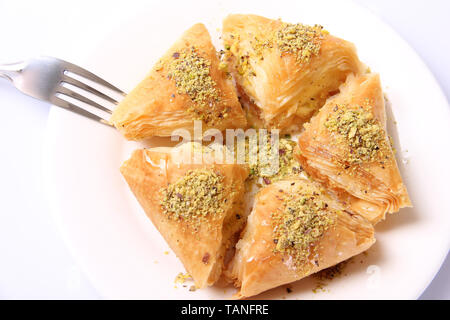 Blick von oben auf die baklawa (Baklava) Platte, enthält fünf Dreieck Baklava Stücke auf eine weiße, runde Platte, mit geerdetem Pistazien, Gabel auf einem Sid gekleidet Stockfoto