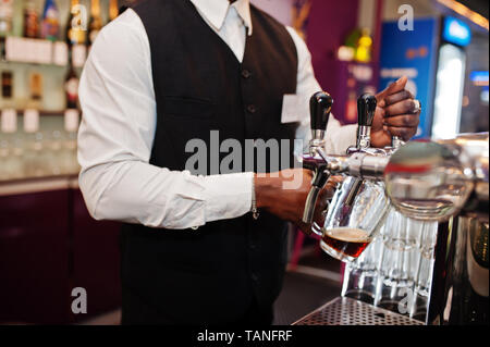 Close up Hände der afrikanischen amerikanischen Barkeeper an der Bar aus frischem Bier in das Glas in der Kneipe tippen Sie gießt. Stockfoto
