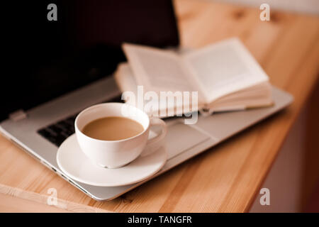 Zu Hause arbeiten als Freelancer Konzept. Tasse Kaffee mit offenem Buch und Laptop im Zimmer. Guten Morgen. Stockfoto