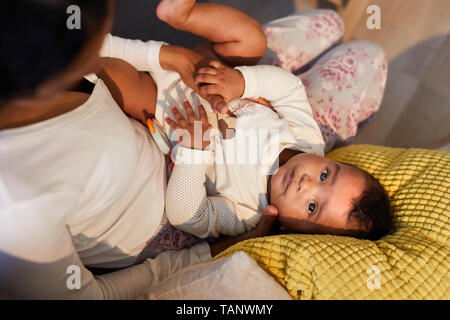 Oben Ansicht von schweren Cute Baby boy in Body liegen auf Kissen und Mütter Beine und Suchen an der Kamera, während Mutter beruhigt Baby Stockfoto