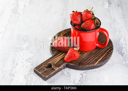Frische Erdbeeren in rot Emaille Tasse auf grauem Hintergrund Stockfoto