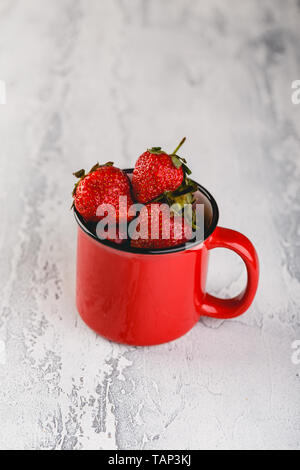Frische Erdbeeren in rot Emaille Tasse auf grauem Hintergrund Stockfoto