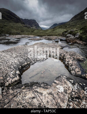 Majestätischen Landschaft Schottlands. Moody Himmel über einen malerischen Berg Tal. Bach mit sauberem Wasser und Felsen in Glencoe, Scottish Highlands. Schönheit in der Natur. Stockfoto