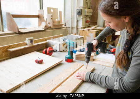 Junge Frau mit elektrischer Schraubenzieher auf ein Stück Holz in der Werkstatt Stockfoto