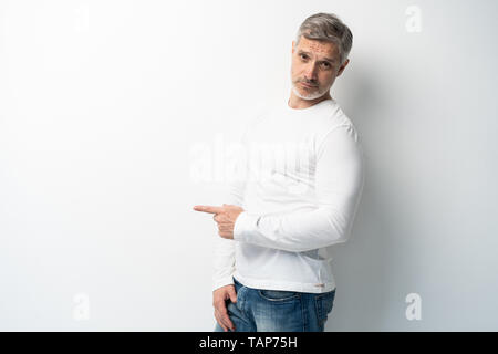 Stattliche mittleren Alters älterer Mann präsentieren und zeigte mit der Hand in die Kamera schaut auf weißem Hintergrund Stockfoto