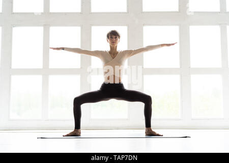 Junge attraktive Yogi frau yoga Konzept, in Malasana Übung sitzen, Girlande darstellen, Arbeiten, Sportkleidung tragen, volle Länge Stockfoto