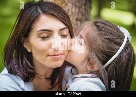 Adorable vier Jahre alt, süße kleine Mädchen küsst ihre Mutter mit Liebe. glückliche Familie auf einer Sommerwiese. Kleines Mädchen Kind baby Tochter umarmen und küssen Stockfoto