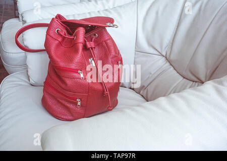 Einer Frau, die Koralle - farbige Rucksack steht auf einem weißen Leder Sofa in der Halle. Dinge zu reisen. Stockfoto