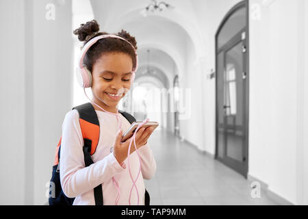 Schöne, hübsche Schulkind in Weiß sweatshirt mit Schule Rucksack stand auf dem Flur der Schule. Süßes schulmädchen Musik hören mit Kopfhörern während der Pause. Stockfoto