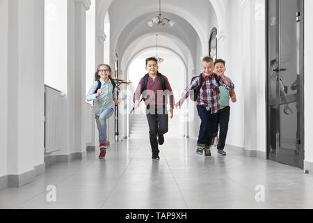 Gruppe von fröhlicher, positiver Schulkinder in langen Flur der Schule läuft. Jungen und Mädchen lachend, in der Pause zwischen den Unterrichtsstunden. Mitschüler lächelnd und ausgeführt wird. Stockfoto