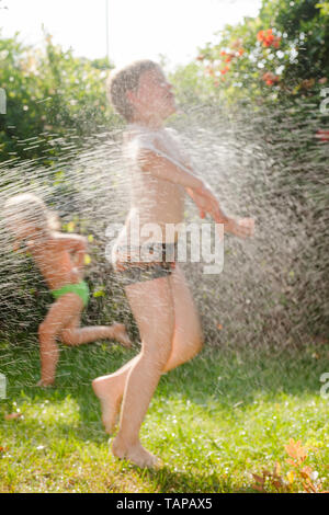 Glückliche Kinder Spaß palying mit Rasen Sprinkler im Sommergarten - Sommerferien Konzept Stockfoto