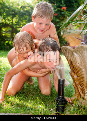 Glückliche Kinder Spaß palying mit Rasen Sprinkler im Sommergarten - Sommerferien Konzept Stockfoto