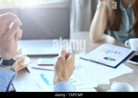 Selektiver Fokus auf Unternehmen Arbeitnehmer Hände. Männliche Arme tun erklären, Gesten und metallic Kugelschreiber halten. Frau in Blau Trendige Bluse etwas schreiben Stockfoto