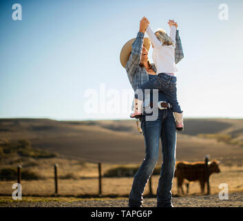 Bäuerin freudig heben ihr Kleinkind in die Luft, während Sie auf der Ranch. Stockfoto