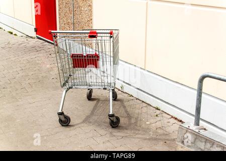Leer Warenkorb in der Nähe der Supermarkt an der Wand. Parken am Supermarkt. Shopping Symbol. Metall Warenkorb. Stockfoto