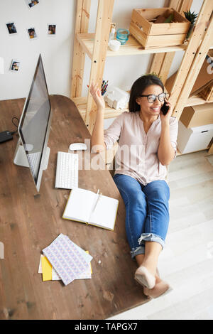 Oben Ansicht Portrait von lächelnden gemischten Rasse Frau spricht über das Telefon beim Sitzen am Schreibtisch im Büro zu Hause, die Füße auf dem Tisch, kopieren Raum Stockfoto