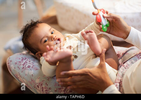 Close-up von Neugierigen niedlichen Baby mit ratty Haare liegen auf Mütter Knie berühren und eigenen Fuß, Mutter spielt mit Baby Stockfoto