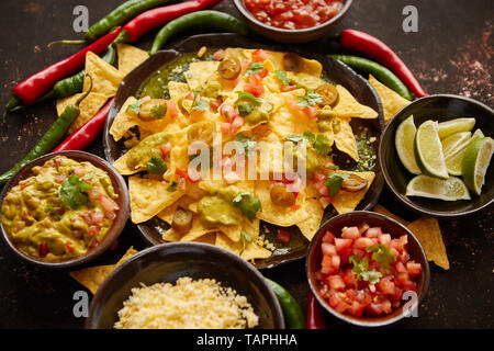 Frischer gelber Mais Nacho Chips garniert mit geschmolzenem Käse, Paprika und Tomaten in einer handgemachte Keramikplatte auf rostigen Tabelle Stockfoto