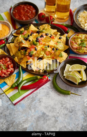 Mexikanische nachos Tortilla Chips mit schwarzen Bohnen, Tomaten, jalapeno, Guacamole, Salsa, Käse und Bier botteled. Auf einem Tisch platziert. Stockfoto