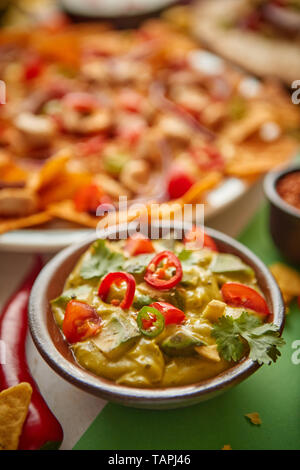 Nahaufnahme auf Guacamole dip in Keramik Schüssel mit verschiedenen frisch zubereitete Mexikanische Lebensmittel Sortiment in den Rücken. Auf bunten Tisch gelegt. Mit Nachos, Tacos Stockfoto