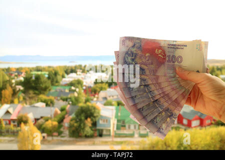 Die weibliche Hand, die eine Reihe von Argentinischen 100 Pesos Rechnungen (zurück) mit verschwommenen El Calafate Stadt im Hintergrund, Argentinien, Südamerika Stockfoto