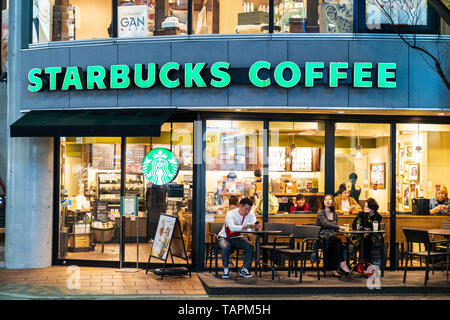 Kumamoto. Im nächtlichen Shimotori Einkaufspassage. Menschen innerhalb und außerhalb von Starbucks Coffee Shop sitzen. Abend mit Gebäude beleuchtet. Stockfoto