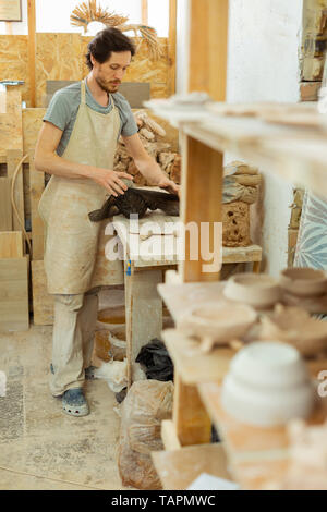 Entschlossener Mann. Professionelle Keramik Master aus Stück frischen Ton aus schwarzem Kunststoff Beutel Stockfoto