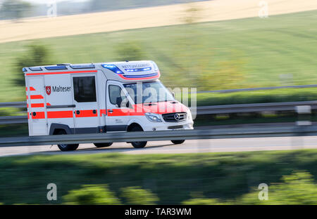 Leuna, Deutschland. 19 Mai, 2019. Ein Malteser Ambulanz Antriebe mit blauem Licht von der Unfallstelle mit einem Trainer. Mindestens eine Person getötet worden und zahlreiche Menschen ernst in den schweren Unfall auf der Autobahn 9 in der Nähe von Leipzig verletzt. Der Bus der Firma Flixbus der Fahrspur auf der A 9 in Richtung München links und umgeworfen. Mehr als 70 Passagiere an Bord waren zum Zeitpunkt des Unfalls. Die A9 wurde vollständig in beide Richtungen an der Unfallstelle geschlossen. Kredite: Jan Woitas/dpa-Zentralbild/dpa/Alamy leben Nachrichten Stockfoto