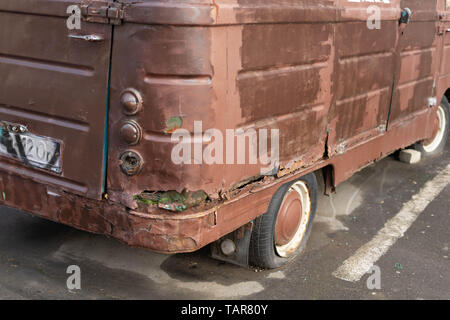 Eine alte rostige Minibus mit einem platten Reifen steht auf einer Straße der Stadt. Stockfoto