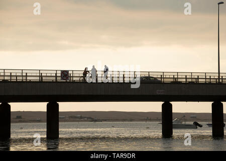 Ein Radfahrer und Fußgänger über die Brücke bei Ferry Bridge am Abend im Mai. Die Rückseite der Chesil Beach kann im Hintergrund gesehen werden. Fähre Bri Stockfoto