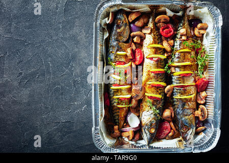 Drei ganze gegrillte Makrele mit Zitronen, Tomaten, Pilze, Gewürze und Kräuter. scomber geröstet in Aluminium Backform, Ansicht von oben, leeren Raum, Stockfoto