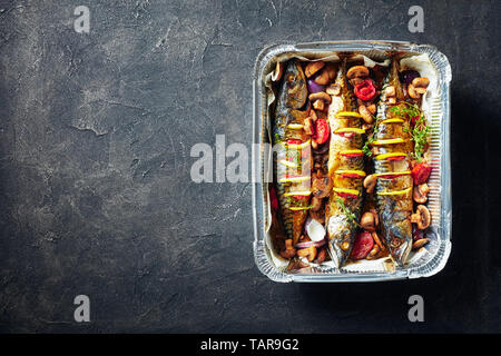 Drei ganze gegrillte Makrele mit Zitronen, Tomaten, Pilze, Gewürze und Kräuter. scomber gebacken in Aluminium Backform mit Pilzen und Tomaten, Anzeigen Stockfoto