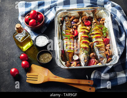 In der Nähe von drei ganze gegrillte Makrele mit Zitronen, Tomaten, Pilze, Gewürze und Kräuter. scomber gebacken in Aluminium Backform mit Pilzen und zu Stockfoto