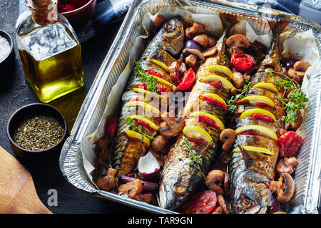 In der Nähe von drei ganze gegrillte Makrelen mit Zitronen, Tomaten, Pilze, Gewürze und Kräuter. scomber gebacken in Aluminium Backform mit Pilzen und t Stockfoto