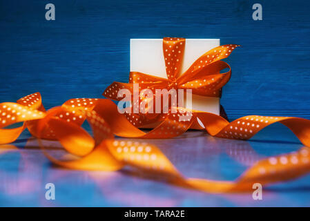 Geschenkbox mit gefleckten Orange Ribbon auf blauem Hintergrund Stockfoto